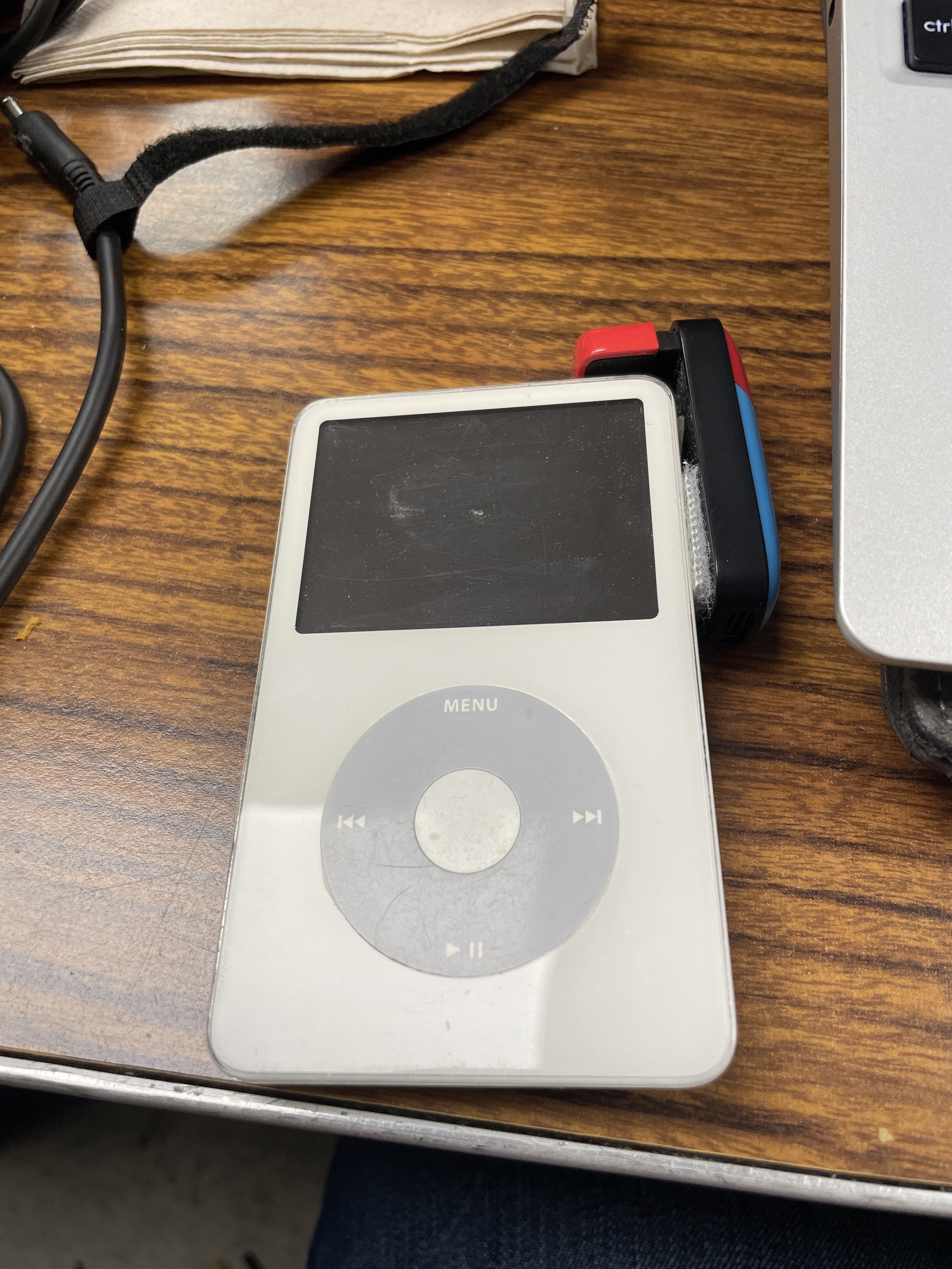 White iPod 5th generation with a blue and red Bluetooth adapter attached to headphone port.